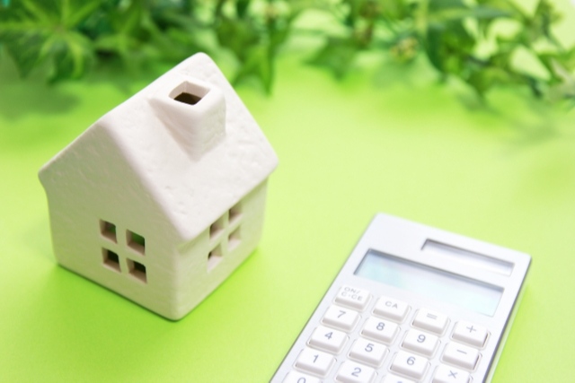 緑のテーブルの上の家の模型と電卓・不動産買取・費用のご相談は株式会社ツインヴィレッジ名古屋
