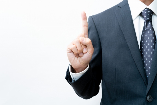 右手人差し指を立てたスーツ姿の男性